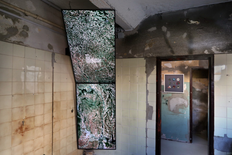 Zwei Bildschirme hängen von der Decke und zeigen Luftaufnahmen der Erde