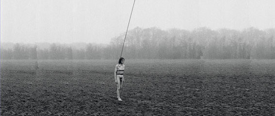 ein nackter Mann läuft über ein Feld und hat einen langen Stab an seinen Körper gebunden